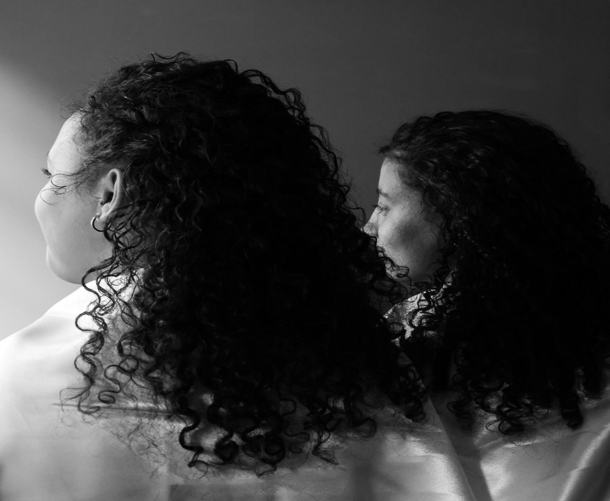 Black and white photo of two people with curly hair looking at each other.